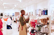 © Ivan Gener/Stocksy - Smiling woman looking at knit hats in a store