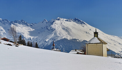 Wall Mural - view on a little chapel in alpine snowcapped mountain in savoie and under blue sky