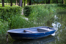 A Blue Boat Stands On A Pond In A Park, A Seagull Sits On A Boat, An Old Boat