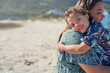 © Caia Image - Portrait happy boy with Down Syndrome over shoulder of mother on beach