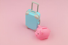 Blue Suitcase With Pink Piggy Bank On Pink Background. Saving Money And Travel Budget Concept.