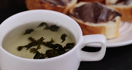 Wall Mural - Green tea brewed in a mug and a baguette with chocolate butter, a delicious sweet dessert with chocolate cream and green hot tea