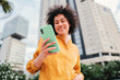 © Jose Calsina - Focus on smartphone. Young hispanic woman typing on cellphone and smiling outdoors. Unfocused happy person using a mobile phone. High quality photo