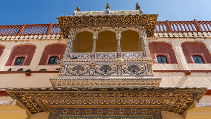 Wall Mural - Details of the architecture of the ancient City Palace in Jaipur. There is a gallery, a balcony with columns and arches. Decorations - peacock drawings, floral ornaments. Blue sky. India