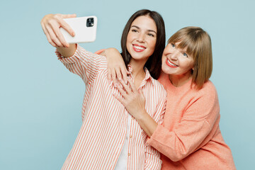 Wall Mural - Elder smiling parent mom with young adult daughter two women together wear casual clothes doing selfie shot on mobile cell phone hug cuddle isolated on plain blue cyan background. Family day concept.