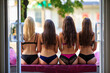 Portrait of four young slim sexy girls sitting in a row shot from behind through the doorway showing their butts and demonstrating lingerie