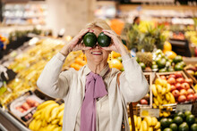 A Goofy Old Woman Is Playing With Avocado And Making Faces At The Supermarket.