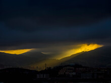 Silhouette Of Residential Buildings On Mountain Range With Dark Clouds And Sunlight