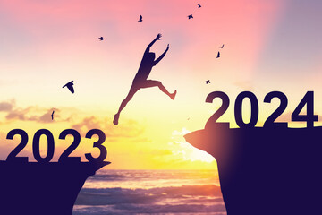 Wall Mural - Silhouette man jumping between cliff with number 2023 to 2024 and birds flying at tropical sunset beach. Freedom challenge and travel adventure holiday concept.