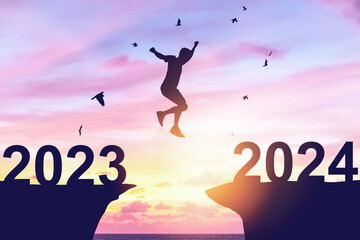 Canvas Print - Silhouette man jumping between cliff with number 2023 to 2024 and birds flying at tropical sunset beach. Freedom challenge and travel adventure holiday concept.