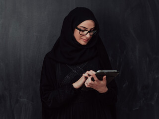 Wall Mural - Young modern muslim business woman using smartphone wearing hijab clothes in front of black chalkboard