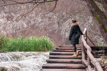 The Girl Stands On A Wooden Bridge And Looks At The Waterfall