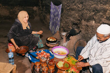 Berber Family Sitting In Old Kitchen Preparing Traditional Moroccan Food. Berber Vintage Kitchen With Black Paint Made With Wood Smoke, Ethnic Group From North Africa.
