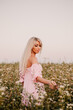 © Volodymyr - Vertical photo blonde woman posing in the big endless field of daisies in summer evening. Lady wear pink dressed, looking aside smiling, touching the plant green blossoming flower. Moody atmosphere