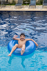 Brazilian 9 years old in the pool, making a face, on a buoy, on a sunny day.