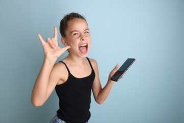 Little emotional teenage girl in pink shirt 11, 12 years old on an isolated blue background with a tablet in her hands.Children's studio portrait. Place the text to copy the place for the inscription