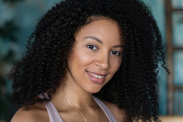 Wall Mural - Middle-aged curly Brazilian woman posing over painted green plant blue background. Looking at camera.