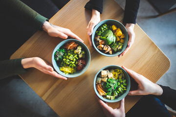 Healthy breakfast. Three friends are holding a bowl. Fresh salad with avocado, grains, beans, vegetables and seafood close-up. Superfood, clean eating, diet food concept