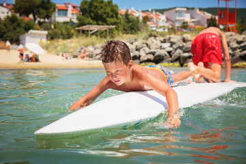 Cheerful teenage boy lying on a swimming board. Happy european family having fun floating on a swim board in the sea on a hot summer day