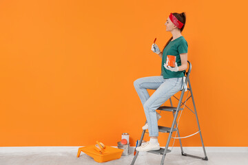 Poster - Designer with painting equipment sitting on folding ladder near freshly painted orange wall indoors, space for text