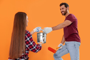 Wall Mural - Man taking can of paint from woman near orange wall. Interior design