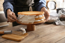 Woman Smearing Sides Of Sponge Cake With Cream At Wooden Table, Closeup