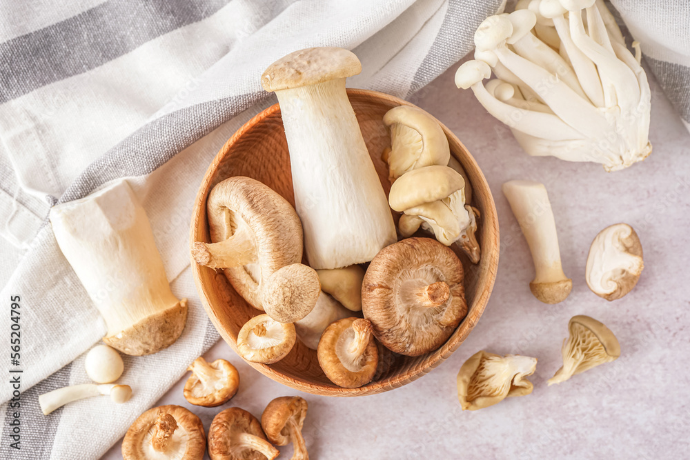 Wooden bowl with fresh mushrooms on light background