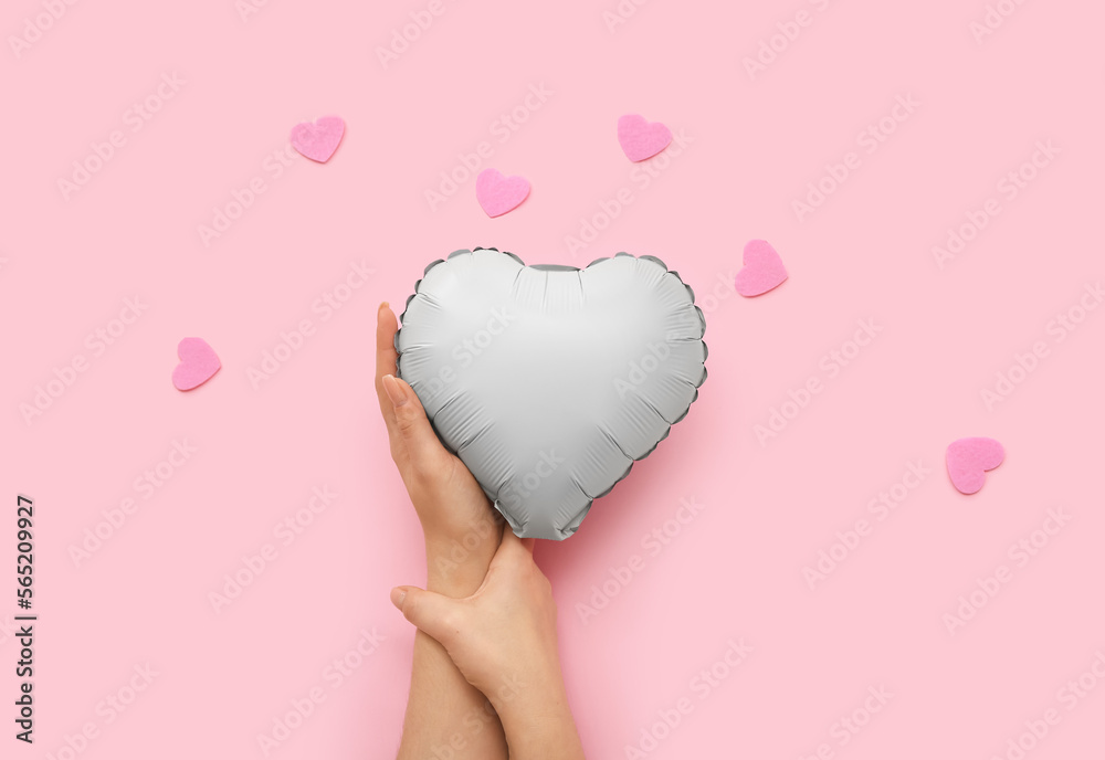 Female hand with heart shape balloon and decor on pink background. Valentine's Day celebration