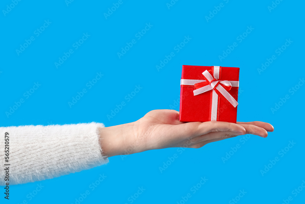 Female hand holding gift on blue background. Valentine's Day celebration