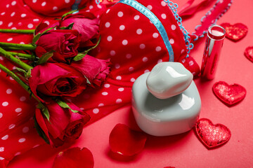 Perfume with lipstick, female underwear, hearts and roses for Valentine's day on red background, closeup