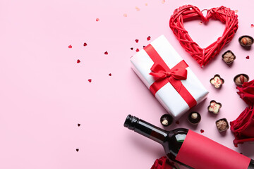 Bottle of wine, chocolate candies, heart, rose flowers and gift on pink background. Valentine's Day celebration