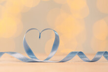 Heart Made Of Satin Ribbon On Table Against Blurred Lights. Valentine's Day Celebration
