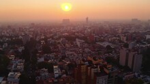 Awesome Dynamic Wide Establishing Shot Of Mexico City At Sunset. In Frame Yellow Orb From The Sun Shining Through The Smog.