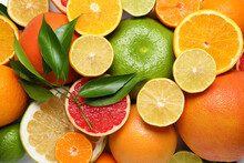 Different Citrus Fruits With Fresh Leaves As Background, Top View