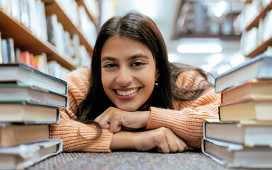 Portrait, Indian woman on floor and books to relax, smile and hobby for learning, growth and education. Student on ground, female or academic in library, knowledge and rest after studying and college