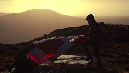 Wall Mural - A man pitching a wild camping tent in idyllic sunset mountain conditions