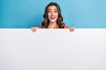 Photo portrait of young pretty girl hiding behind white wall excited promo dressed stylish orange clothes isolated on blue color background