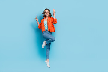 Sticker - Full size photo of young pretty girl jumping excited showing double v-sign dressed stylish orange clothes isolated on blue color background