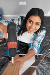 Overhead shot of young Indian woman drilling into wood during home renovation