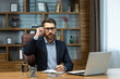© Liubomir - Serious thinking boss inside the office portrait of a mature businessman with a beard and glasses, the man is looking at the camera with concentration, working with documents on a laptop at the table