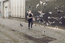 Running On The Street Between Flying Pigeons - Playful Life Of Positive People In Movement