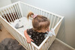 © Cavan Images - High angle of blonde toddler girl in crib bed.