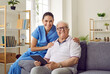 © Studio Romantic - Portrait of smiling nursing home nurse and older man who is learning to use digital tablet. Young friendly Caucasian woman in medical uniform and senior man sitting on sofa and smiling at camera.