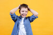 Portrait of a laughing boy holding his head. He’s looking down and away. Yellow background. Front view. Copy space. Suitable for collage and banner making and other design