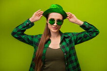 Young Happy Irish Woman In Green Checkered Plaid Shirt With Clover Shaped Glasses Holding Green Party Hat And Looking At Camera Isolated On Green Background.

St Patricks Day Celebrating Concept.