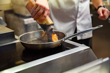 man chef cooking fried salmon fish in frying pan on kitchen