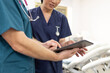 © Austockphoto - Man and woman health care workers standing next to each other while looking at tablet in the clinic