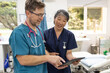 © Austockphoto - Man and woman health care workers  standing next to each other looking at a tablet in the clinic
