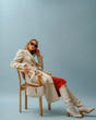 © Victoria Fox - Fashionable confident woman wearing elegant white woolen coat, sunglasses, high leather heeled boots, posing on blue background. Full-length studio fashion portrait. Copy, empty space for text
