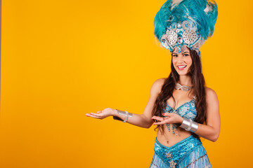 beautiful brazilian woman with queen clothes from samba school, carnival. Feather crown, presenting something to the left.